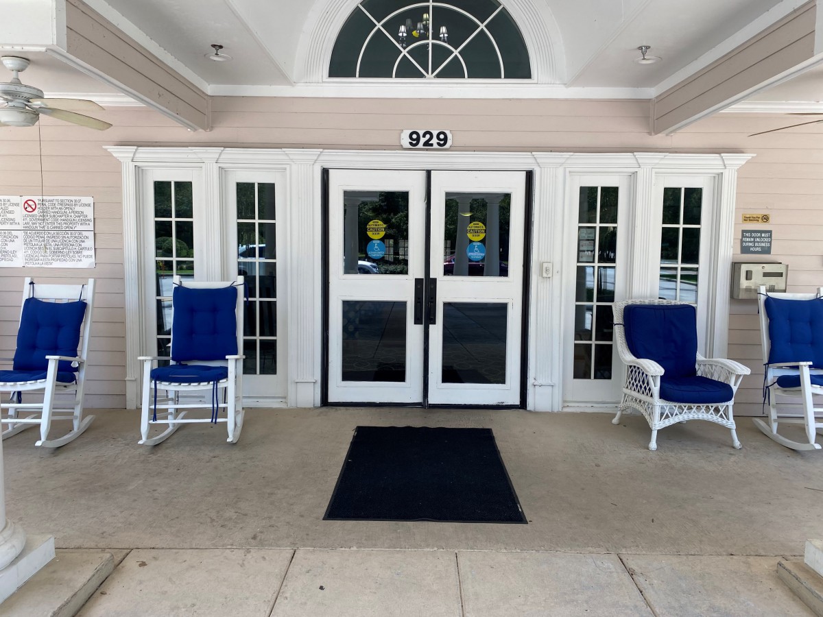 A building entrance with double doors, flanked by two blue rocking chairs.
