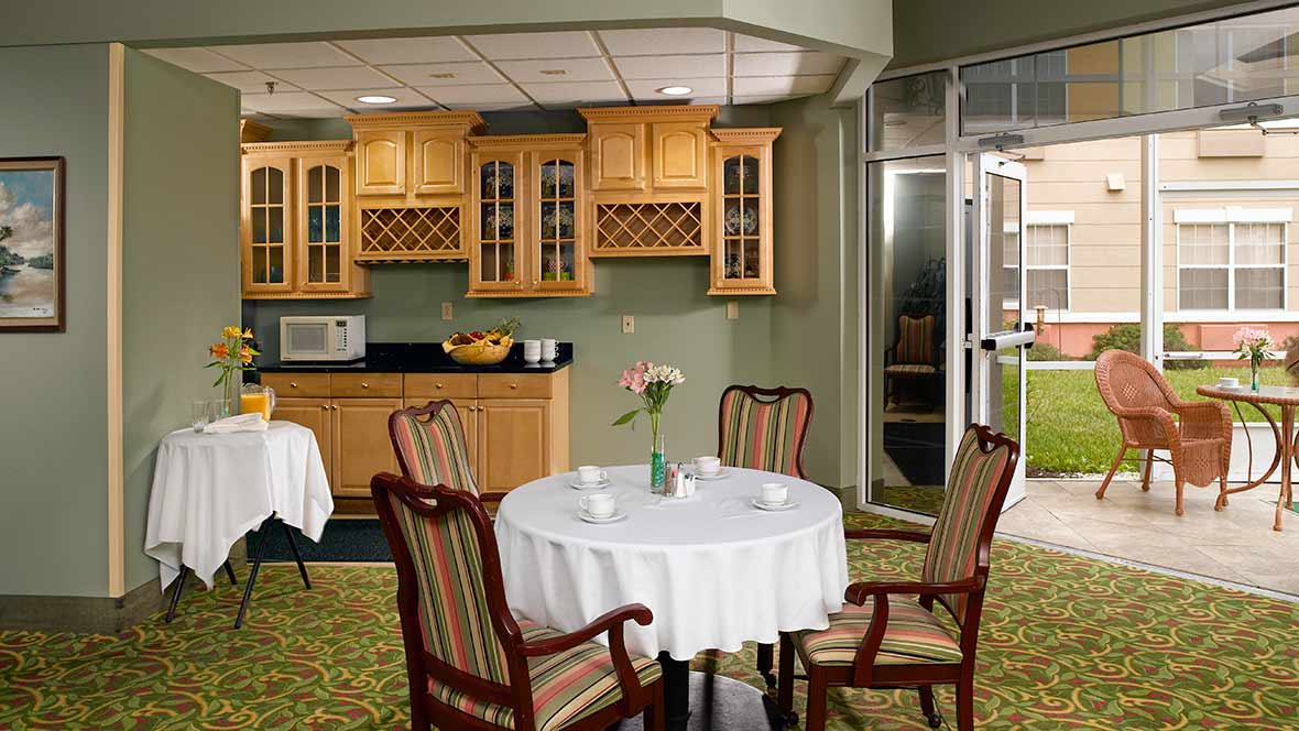 A cozy dining space with a round table, surrounded by wooden chairs, and a small kitchen area in the background.