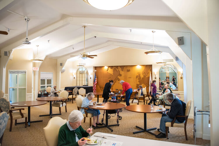 A community dining room with seniors seated at tables, enjoying a meal together.