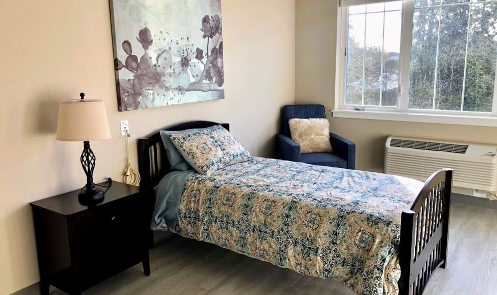 Cozy bedroom with a single bed, patterned bedding, and a comfortable chair by the window.