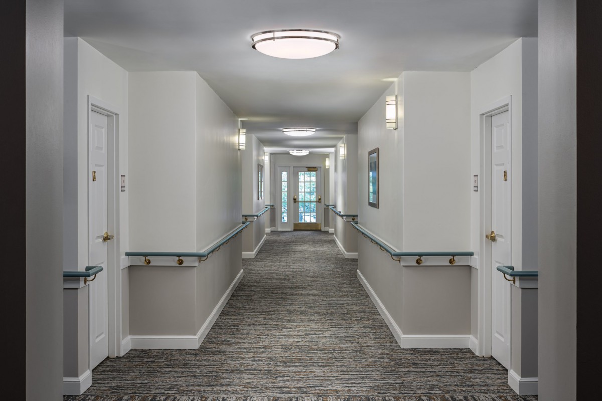 A brightly lit hallway with doors lining both sides and a carpeted floor.