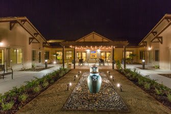 Illuminated building entrance with pathway and decorative pottery at night.