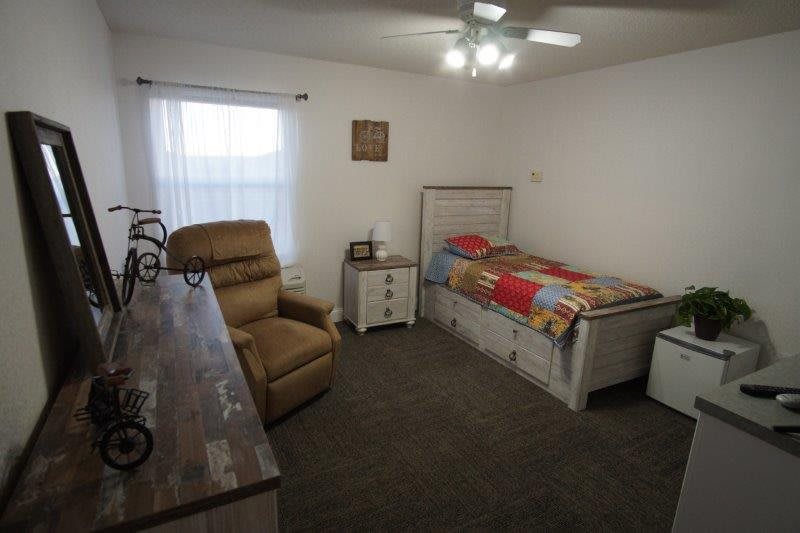 A cozy bedroom with a single bed, recliner chair, and a window letting in natural light.