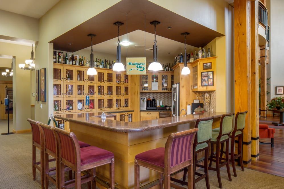 A cozy home bar with wooden accents, illuminated by pendant lights and surrounded by shelves filled with wine bottles.
