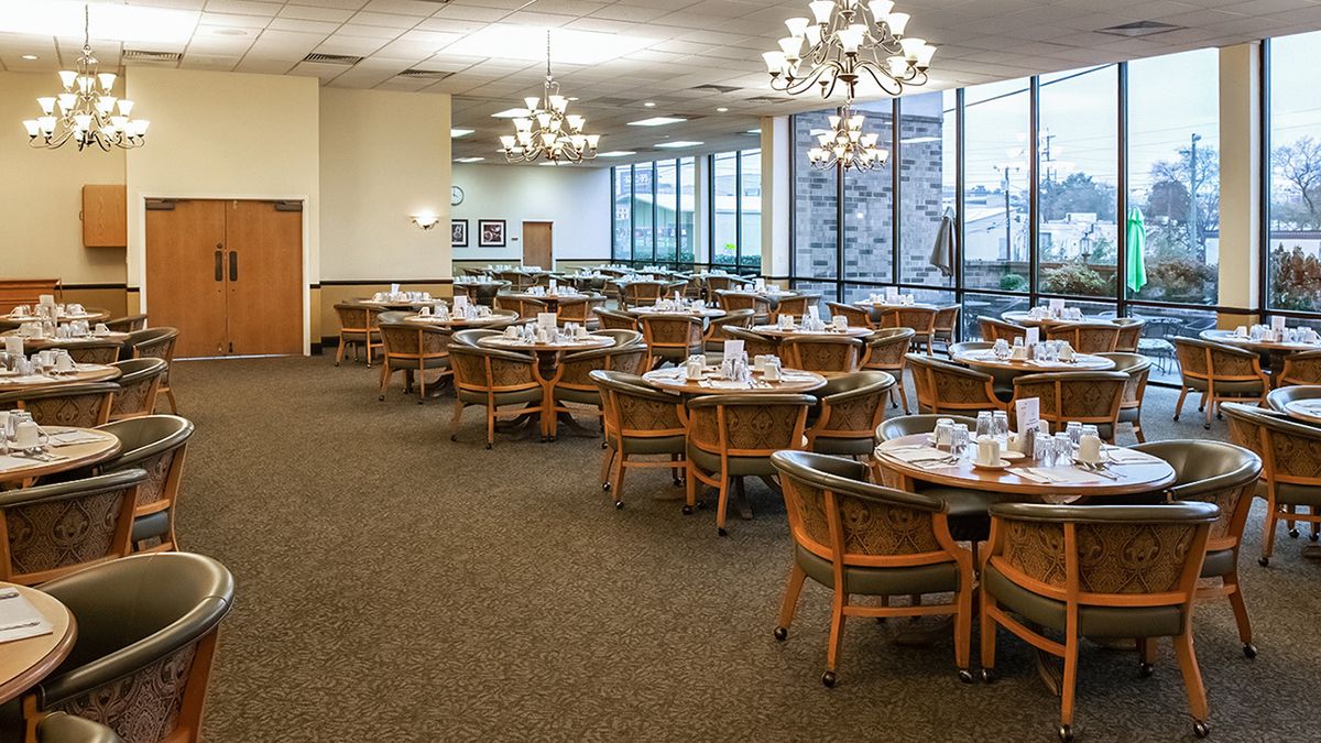 An elegant dining room with neatly arranged tables and chairs, illuminated by chandeliers.