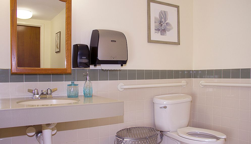 A clean bathroom with a toilet, sink, mirror, and paper towel dispenser.