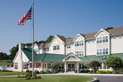A residential-style building with a green roof and an American flag in front, surrounded by well-maintained landscaping.