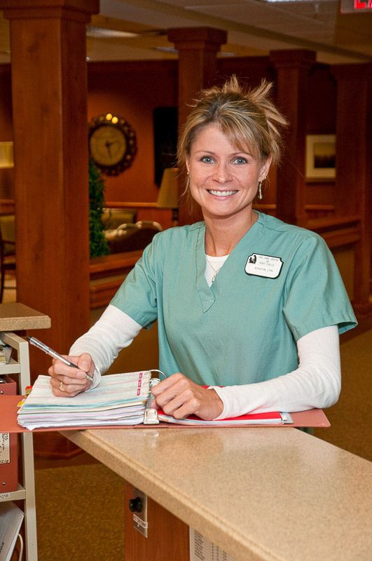 A nurse in scrubs is writing on a clipboard in a healthcare setting.