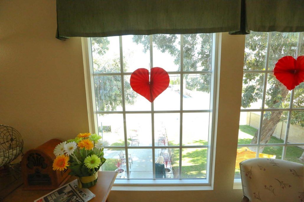 A heart-shaped decoration on a sunlit window with flowers nearby.