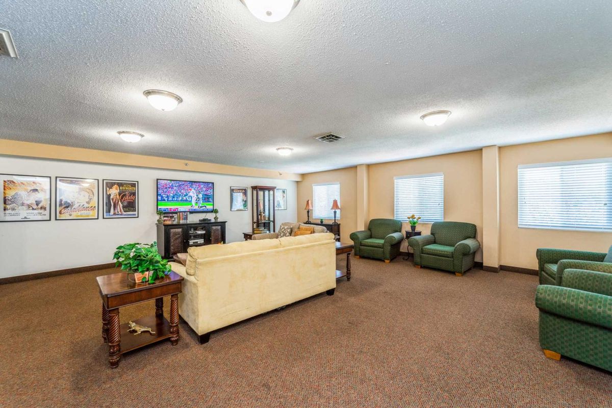 A spacious and well-lit living room featuring a beige sofa, two green armchairs, a television, and tasteful decor.