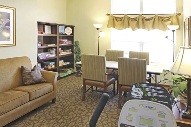A cozy living room with a sofa, bookshelves, a table surrounded by chairs, and a standing lamp.