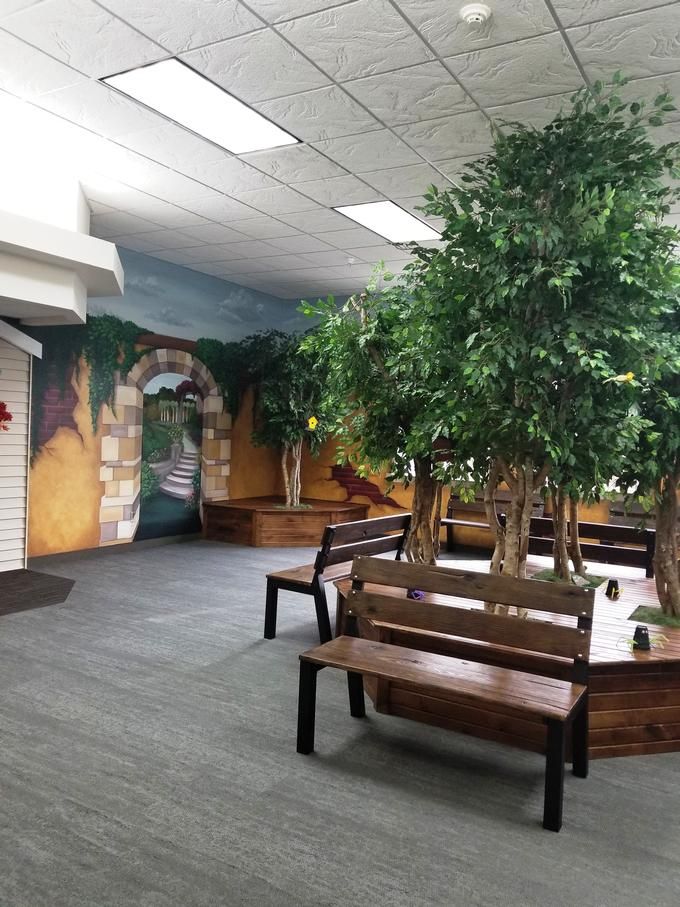 A cozy indoor seating area with benches and artificial trees, complemented by a scenic mural on the wall.