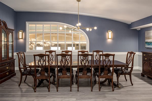A beautifully decorated dining room with a large wooden table and matching chairs, featuring a blue accent wall and an arched window reflecting light from the chandelier.