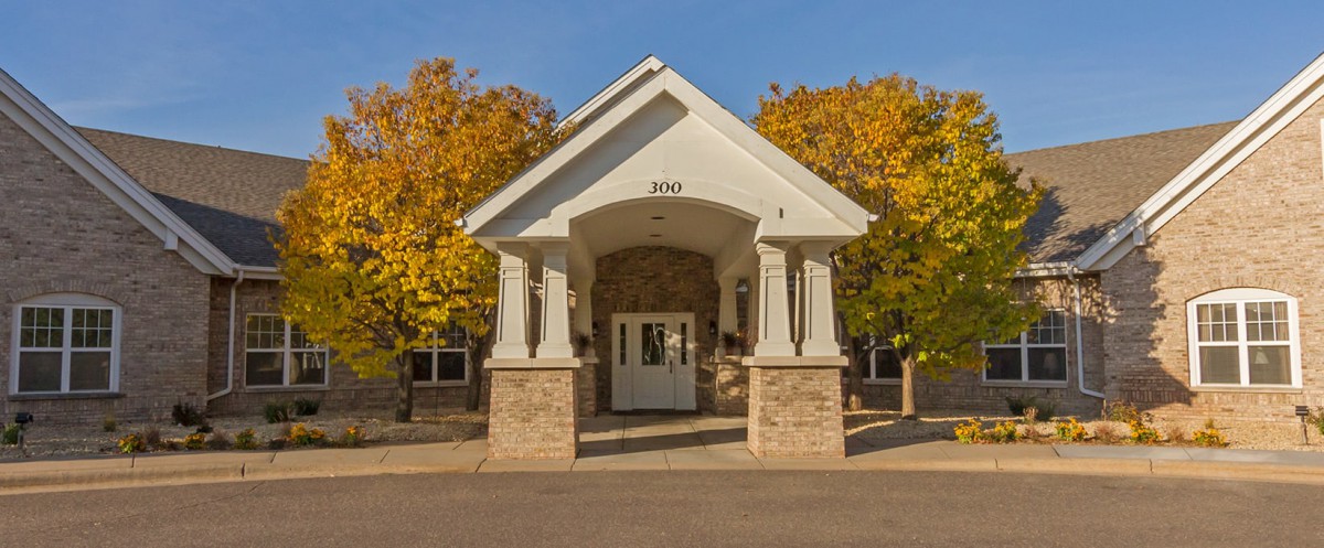 A building entrance with white pillars, surrounded by autumn foliage.