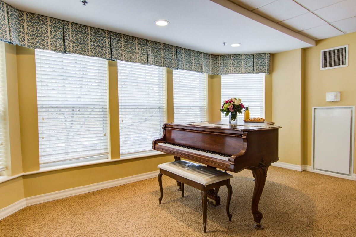 A grand piano placed in a well-lit living room with large windows.