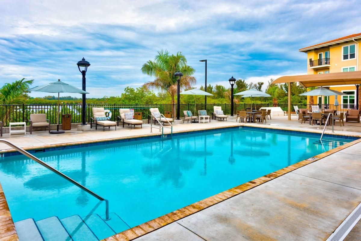 A tranquil outdoor swimming pool area with lounge chairs and umbrellas under a bright blue sky.