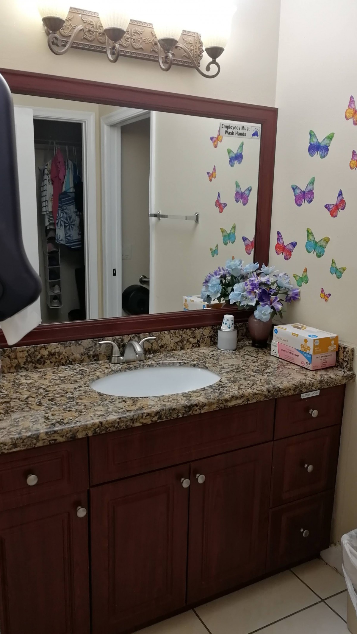A bathroom with a granite countertop, decorated with butterfly decals and a vase of flowers.