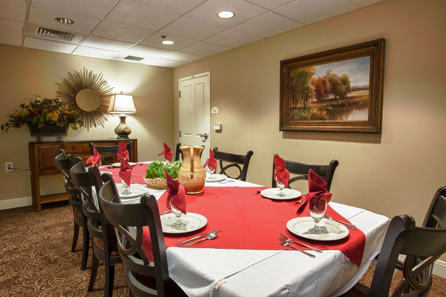 A warmly decorated dining room with a table set for six, featuring a red and white tablecloth and neatly folded napkins.