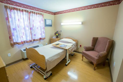 A cozy patient room in a hospital, featuring a bed, chair, and natural light.