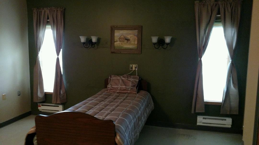 A cozy bedroom featuring a single bed with plaid bedding, surrounded by dark green walls and illuminated by wall-mounted lamps.