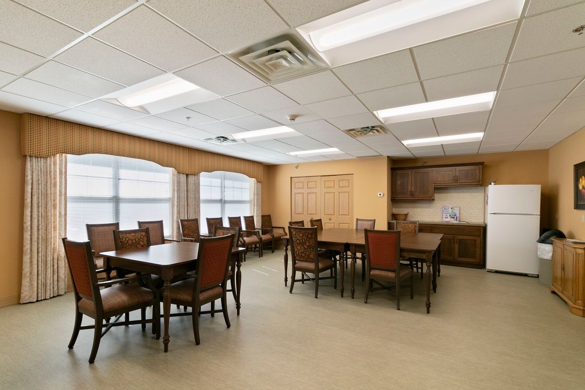 An empty dining room with several tables and chairs, illuminated by ceiling lights and natural light from the windows.