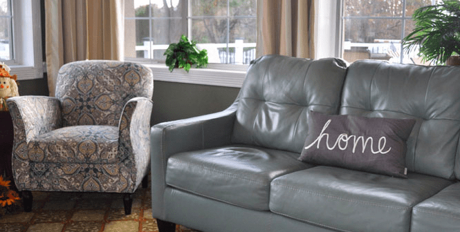 A cozy living room featuring a leather sofa with a decorative pillow and an upholstered armchair near a window.