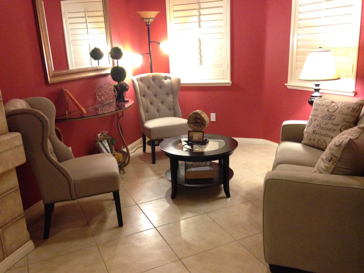 A cozy living room with red walls, featuring comfortable chairs, a sofa, and a coffee table illuminated by lamps.