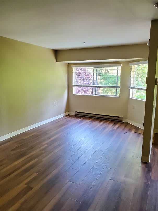 An empty room with hardwood floors and large windows letting in natural light.