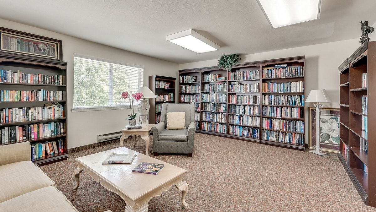 A cozy reading room with bookshelves, an armchair, and a table under soft lighting.