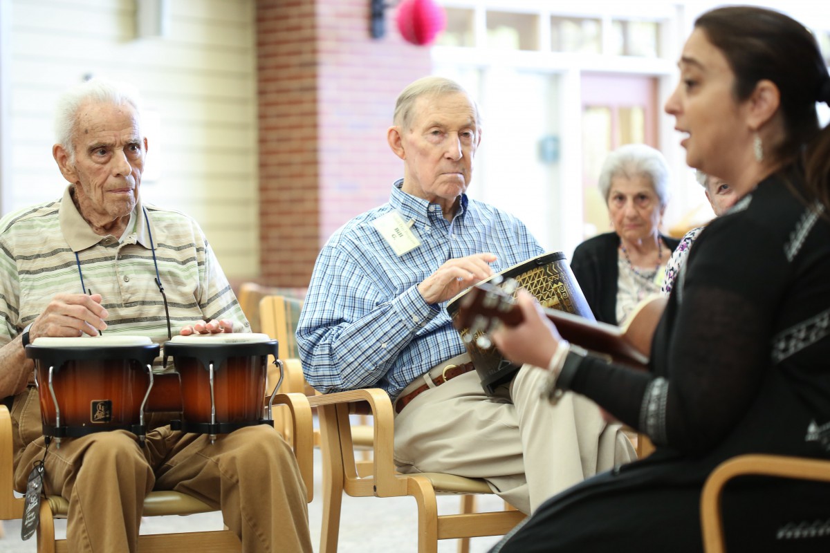 A group of seniors participating in a music session, with one person playing the guitar and another playing the drums.