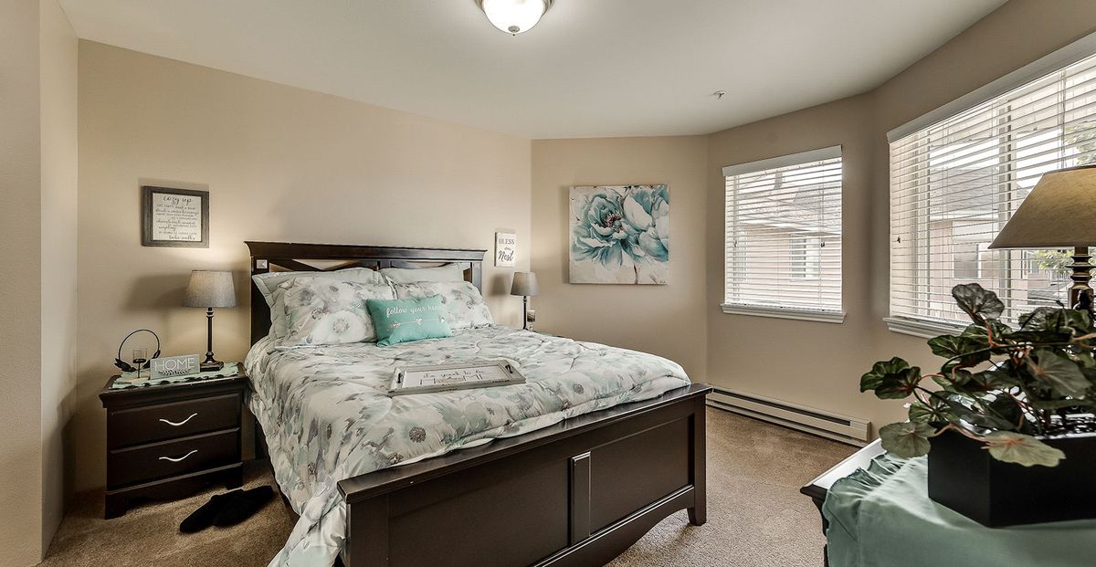 A cozy bedroom featuring a comfortable bed with patterned bedding, artwork on the wall, and natural light coming through the window.