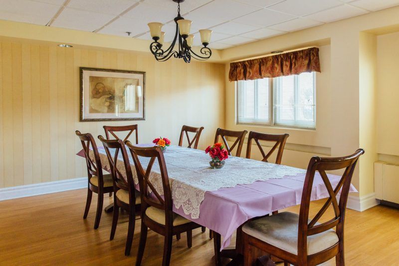A well-lit dining room with a long table covered in a purple tablecloth and floral centerpieces.