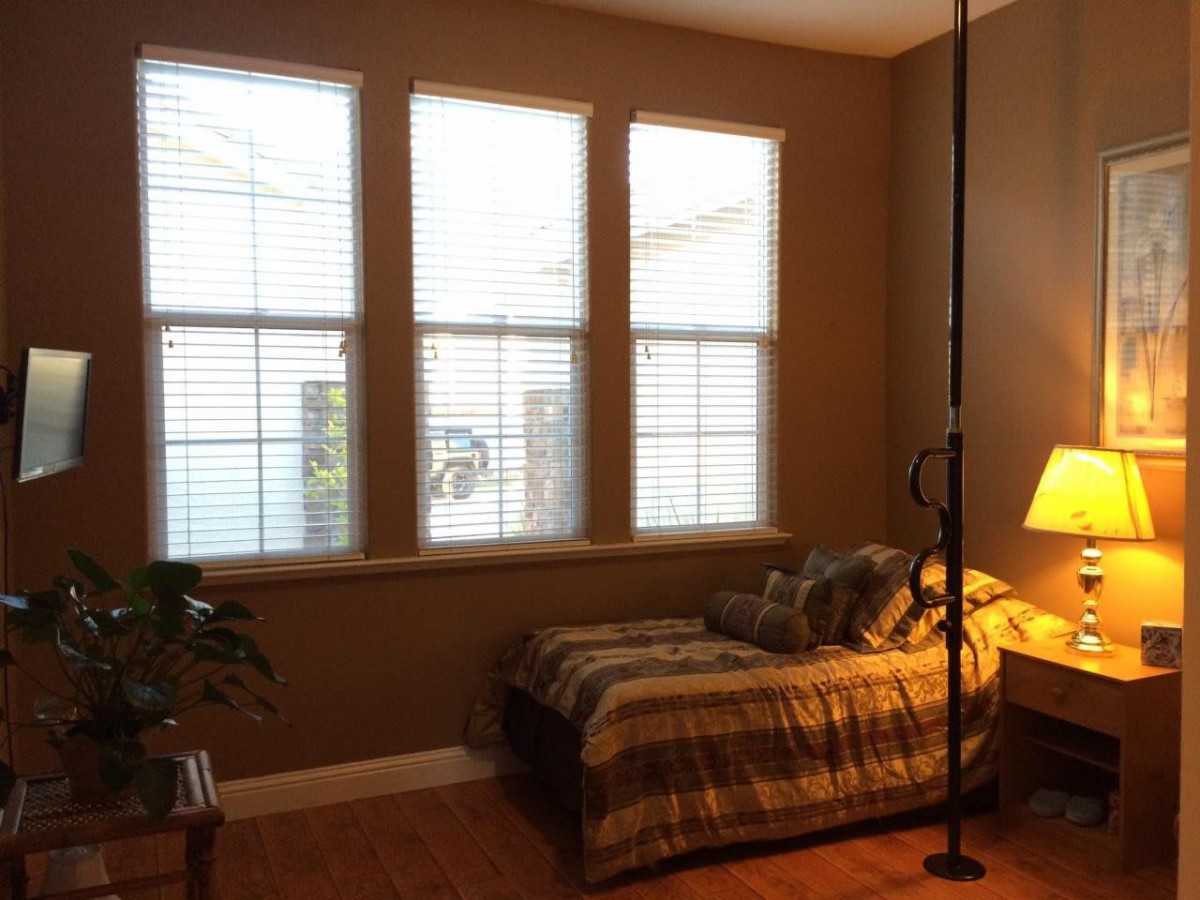 A cozy bedroom with a bed near large windows and a standing lamp.