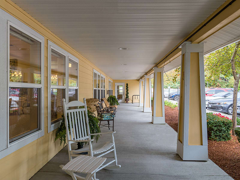A cozy porch with rocking chairs and outdoor seating, featuring columns and large windows.