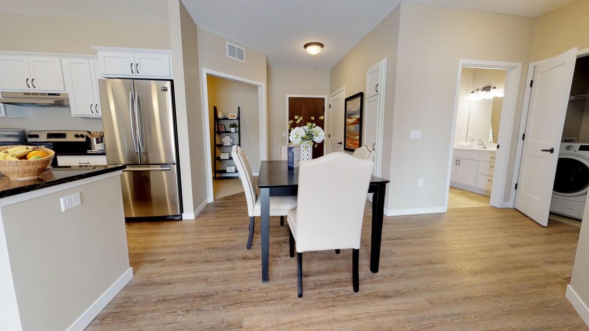 A modern dining area with a black table, beige chairs, and wood flooring next to a kitchen.