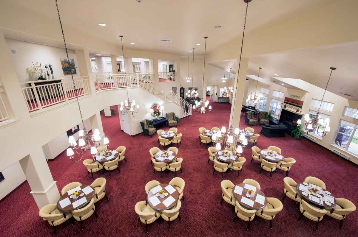 An elegant restaurant interior with tables set on a red carpeted floor and chandeliers hanging from the ceiling.