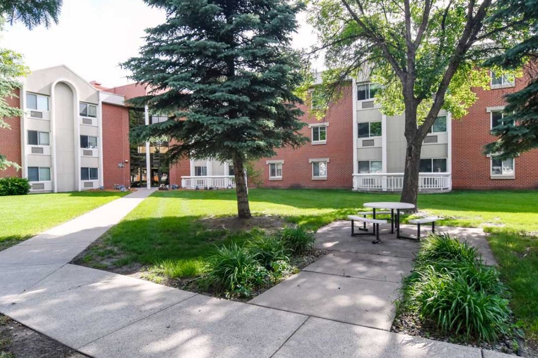 A peaceful residential apartment complex with lush greenery and outdoor seating areas.