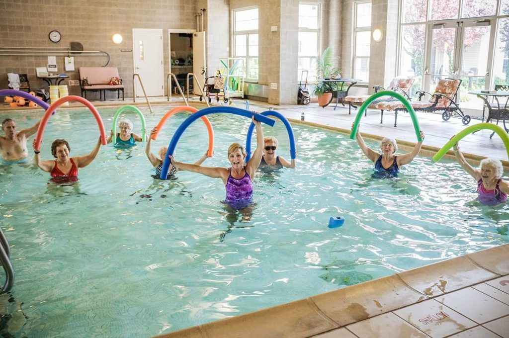 A group of older adults participating in a water aerobics class inside an indoor swimming pool.