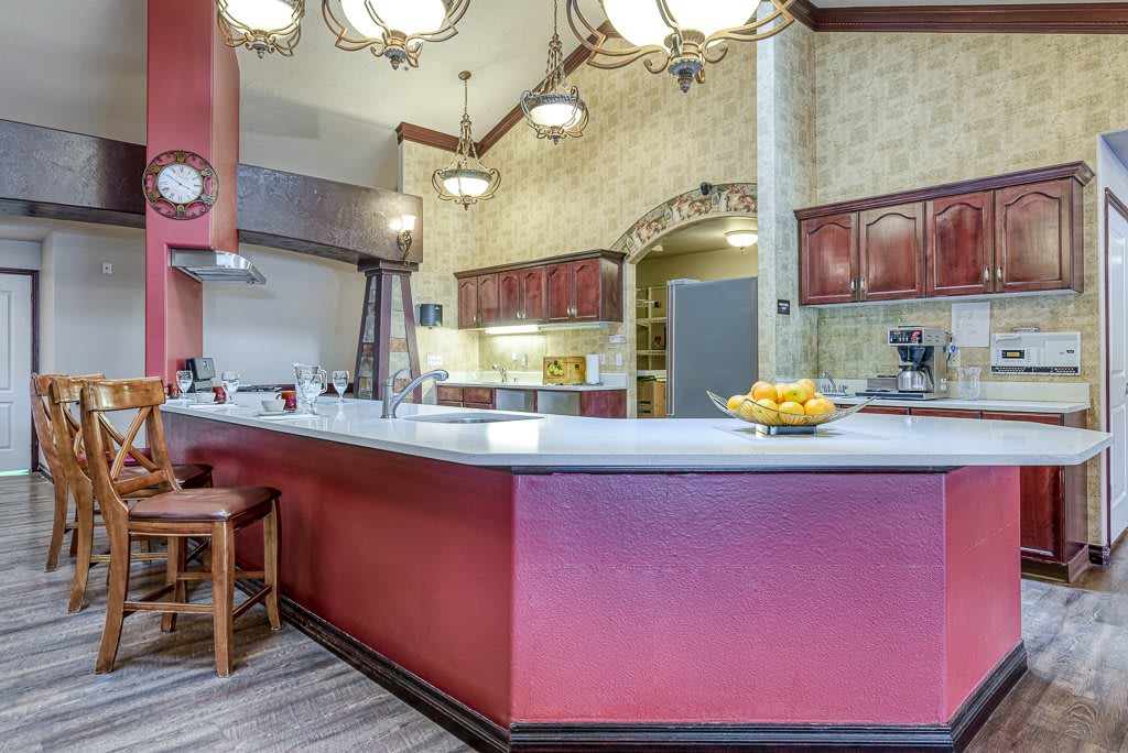 A spacious kitchen with red cabinetry, a large white countertop, and elegant chandeliers.