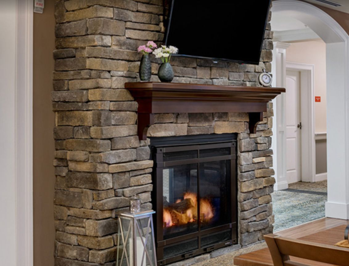 A cozy fireplace with a stone surround, topped by a wooden mantel adorned with vases of flowers and a television mounted above.