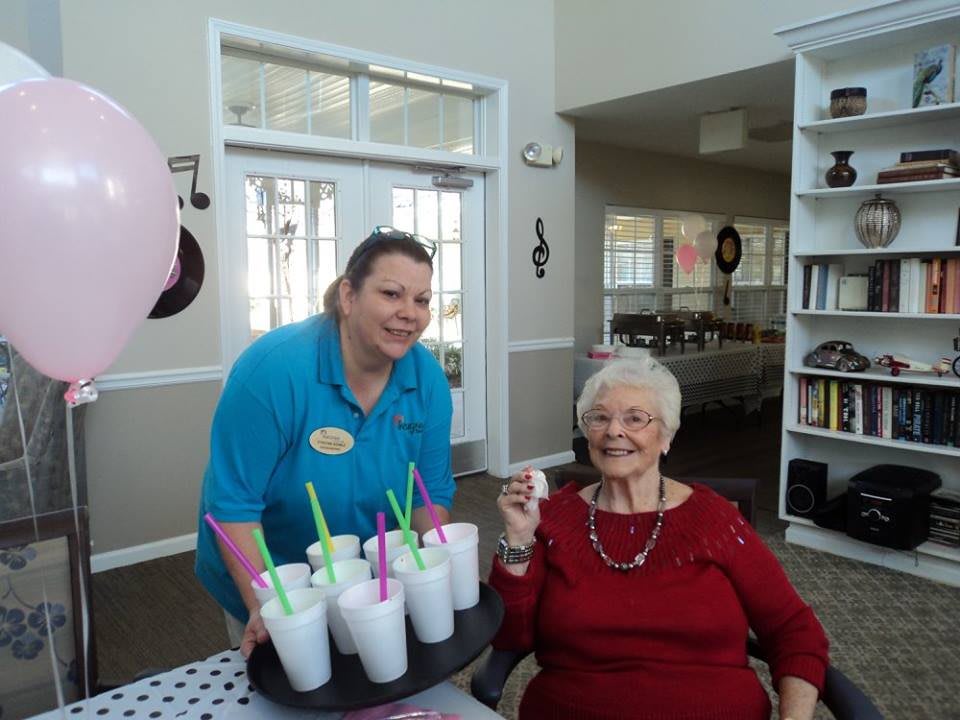 An elderly woman enjoying a celebration with milkshakes served by a staff member.