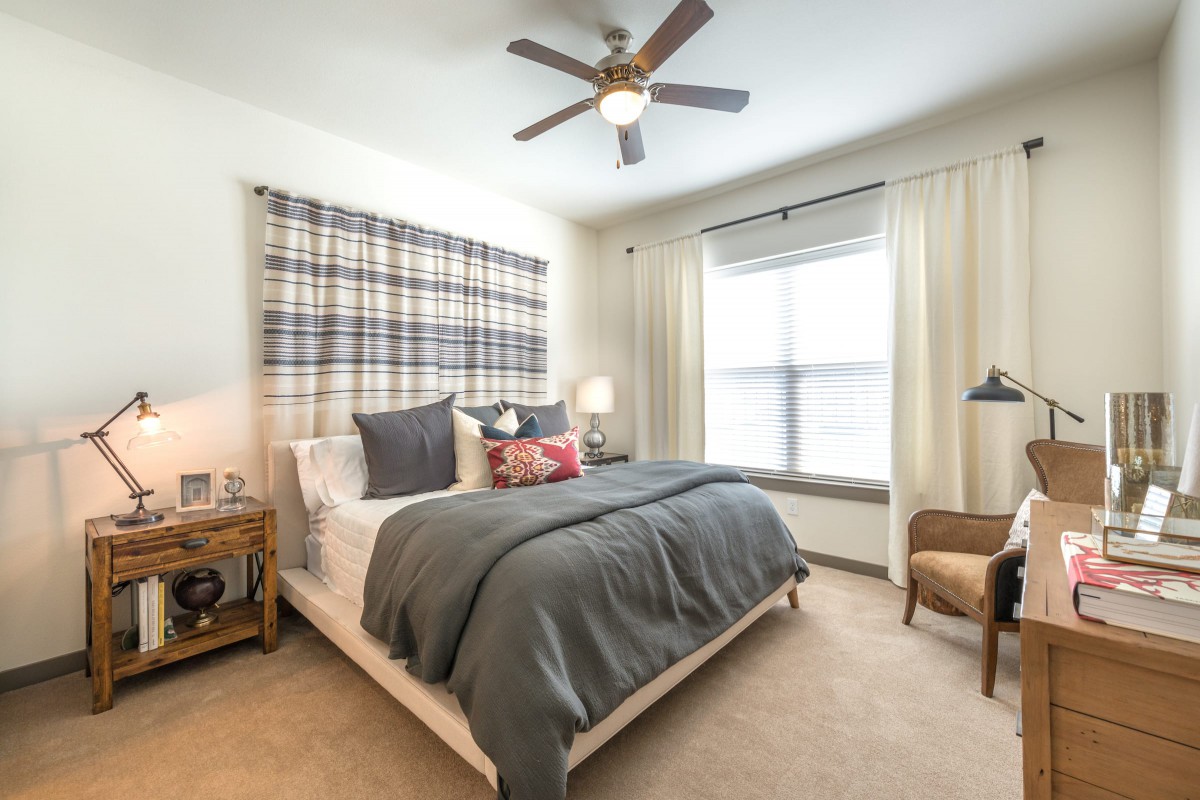 A modern bedroom with a stylish design, featuring a cozy bed, large window with curtains, and a ceiling fan.