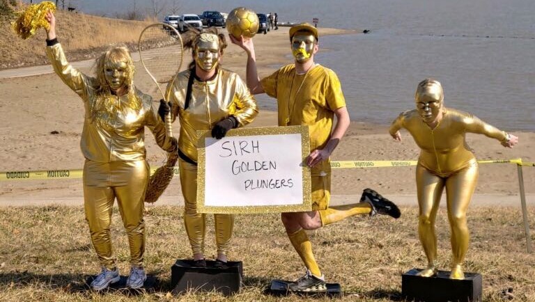 A group of people dressed in gold costumes posing outdoors with a sign that says 'SRH Golden Runners'.