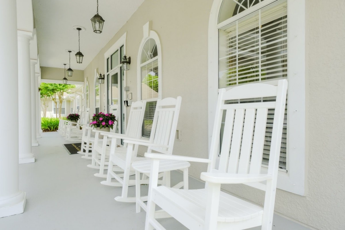 A cozy porch featuring white rocking chairs and hanging lights.