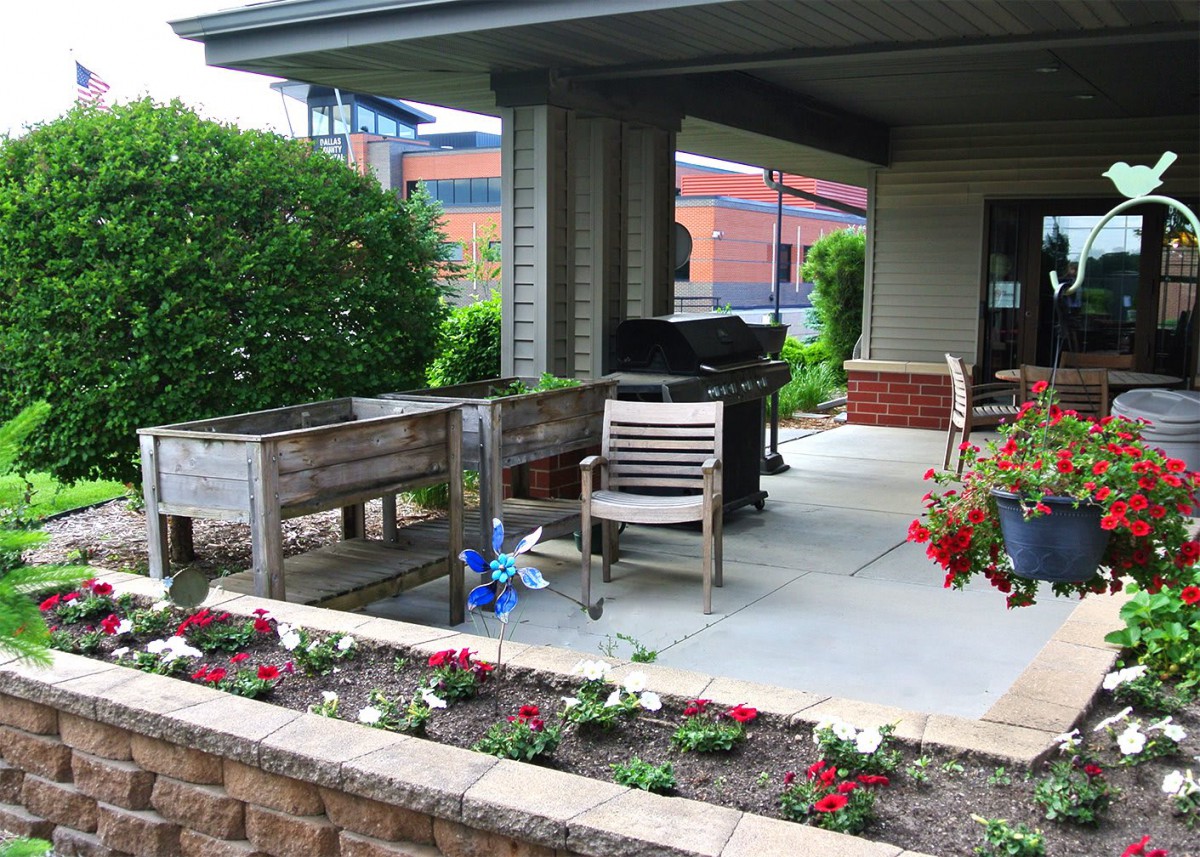 A cozy outdoor patio with gardening planters and seating area surrounded by flowers and greenery.