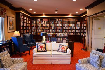 A cozy library room with shelves full of books, comfortable seating, and warm lighting.