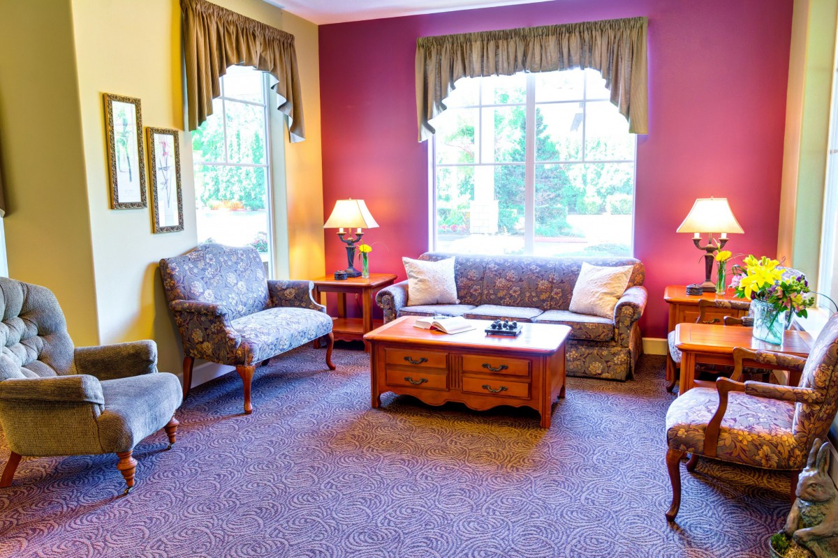 A cozy living room with a sofa, armchairs, and a coffee table, illuminated by lamps near large windows.
