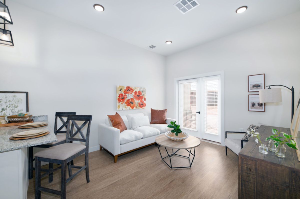 A bright and modern living room featuring a white sofa, colorful cushions, a round coffee table, and decorative wall art.