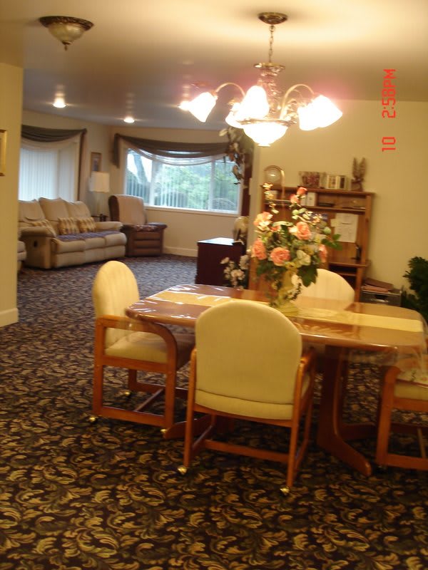 A cozy dining and living area with a table set, chairs, a sofa, and decor including flowers and a chandelier.