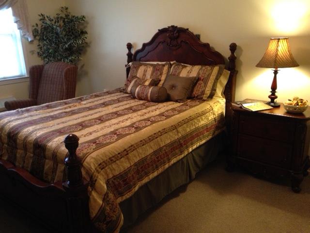 A cozy bedroom featuring a wooden bed with patterned bedding, complemented by a nightstand and lamp.